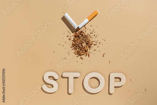 Fotografía Broken cigarette with scattered tobacco with text STOP on beige background