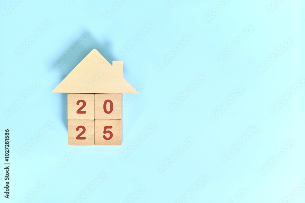Year 2025 home ownership goal and real estate property investment concept. Wooden blocks on blue background with icon.