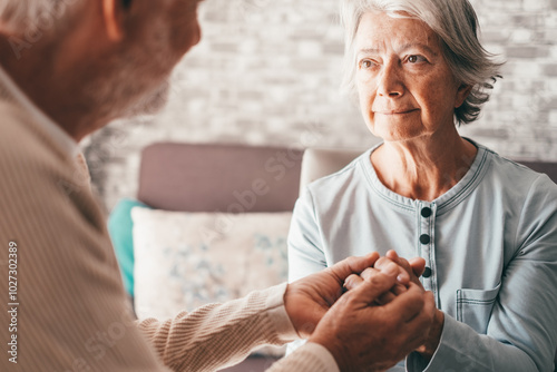 Senior man comforting his depressed sad wife, unhappy elderly woman sitting on sofa at home needed support and care. Two pensioners express their feelings and closeness