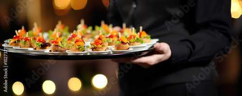 A waiter serving a platter of colorful appetizers at a lively evening event with soft lighting