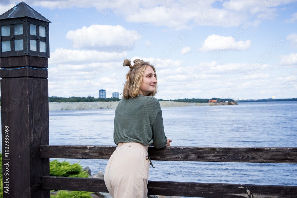 young blond woman in a sweater, portrait, standing on a bridge on the lake, smiling, posing, photosession young blond woman in a sweater, portrait, standing on a bridge on the lake, smiling, posing, photosession