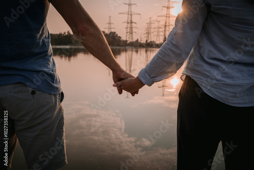 Couple holding hands by a serene lake at sunset with power lines in the background photo