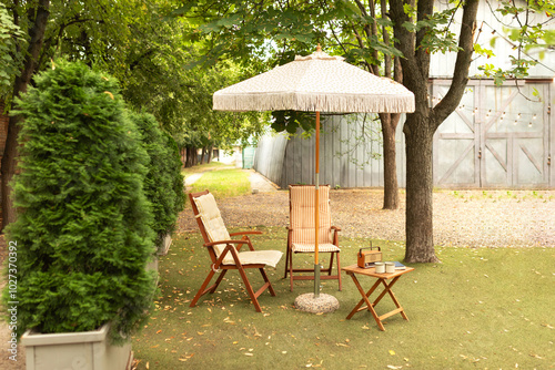 Cozy interior courtyard with table with old radio and sun loungers with umbrella in backyard. Garden furniture for leisure time in nature. Wooden outdoor furniture set for Picnic for campsite. 