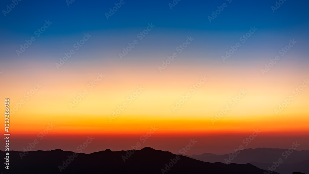 The sky gradient from blue to orange over the mountains. The mountains look like an oriental painting. The sky gradient from blue to orange over the mountains. The mountains look like an oriental painting.