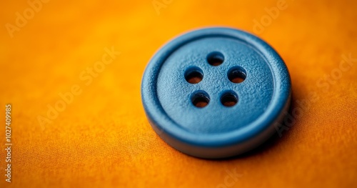 A bright blue button with four holes lays atop a vibrant orange fabric, highlighting sewing craftsmanship and color contrast