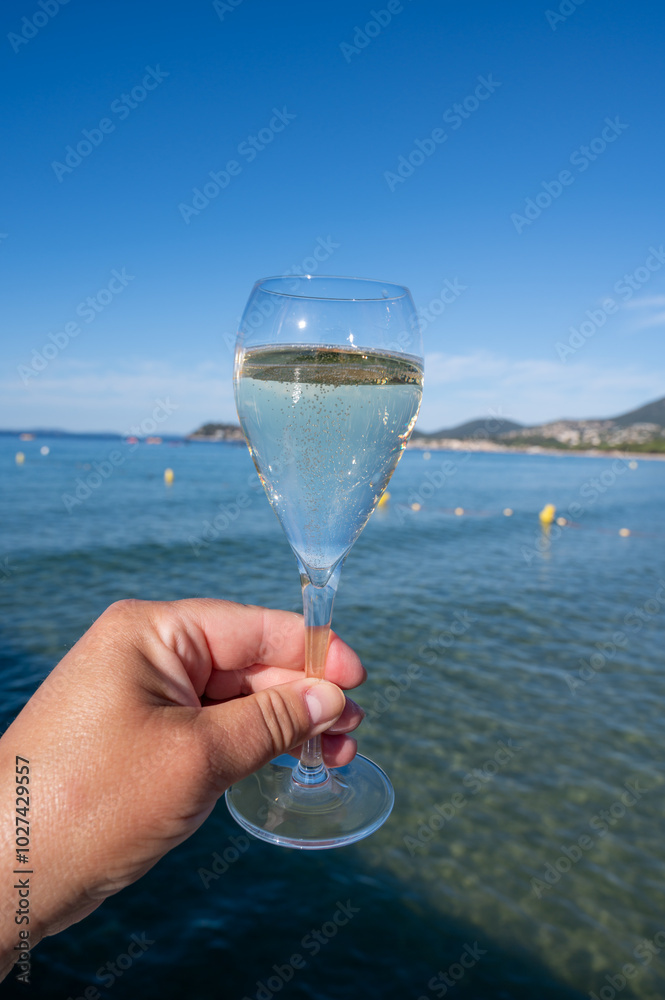 Obraz premium Summer time in Provence, hand with glass of cold champagne cremant sparkling wine on famous Pampelonne sandy beach near Saint-Tropez in sunny day, Var department, France, beach club party