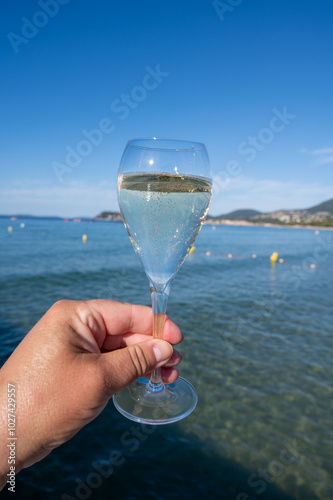 Summer time in Provence, hand with glass of cold champagne cremant sparkling wine on famous Pampelonne sandy beach near Saint-Tropez in sunny day, Var department, France, beach club party