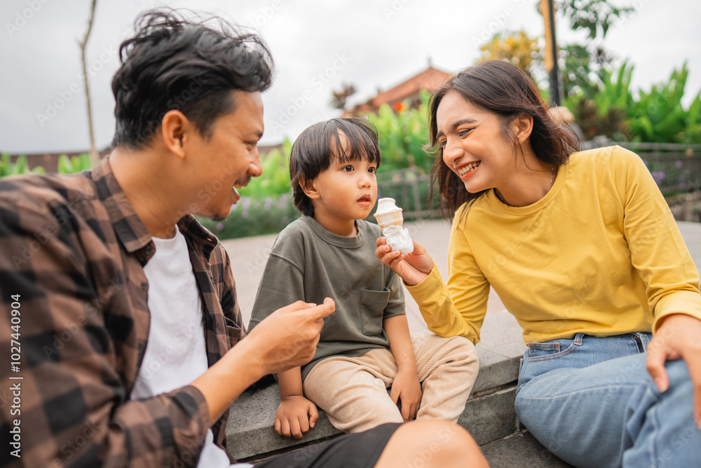 little boy daydreaming while feeding mom ice cream while playing with dad in the park