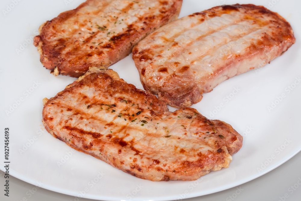 Grilled boneless pork chops with spices on dish, close-up