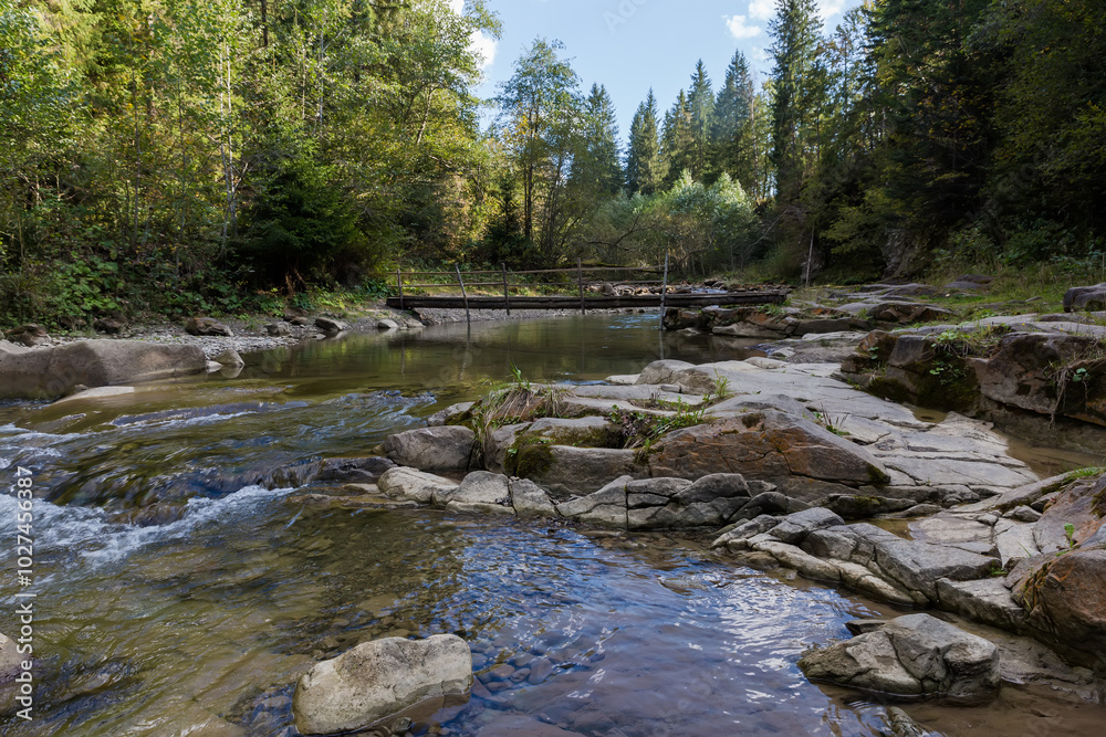 Mountain river section with narrow wooden footbridge at autumn day Mountain river section with narrow wooden footbridge at autumn day
