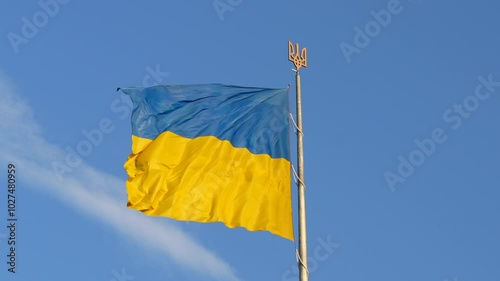 Flag of Ukraine flapping in the wind in slow motion on a flagpole with trizub on top photo