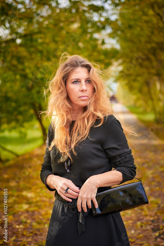 Beautiful woman in black dress and necklace walking in autumn forest. Relaxation concept