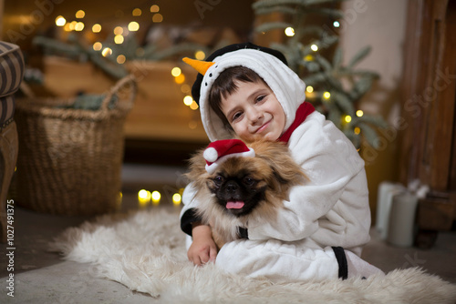 Happy childin snowman pyjamas embraces dog Pekingese celebrates Christmas at home. Christmas time.
 photo