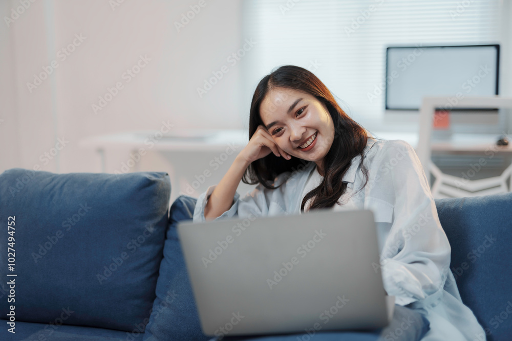 Young asian woman is working from home, enjoying the comfort of her couch while staying productive