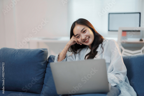 Young asian woman is working from home, enjoying the comfort of her couch while staying productive