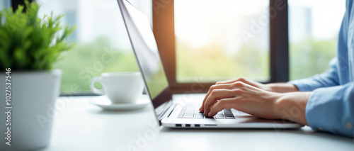 Person typing on a laptop with a coffee cup beside them, set in a bright and modern workspace. The image emphasizes productivity and a comfortable working environment.