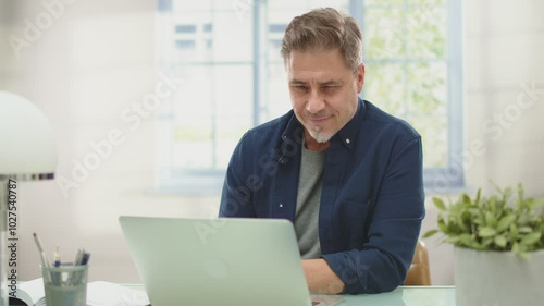 Happy mid adult man working with laptop computer at home, sitting at desk with confident smile. Businessman online form home office, Portrait.