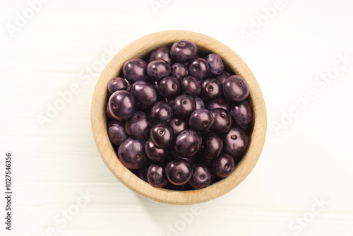 Ripe acai berries in bowl on white wooden table, top view photo