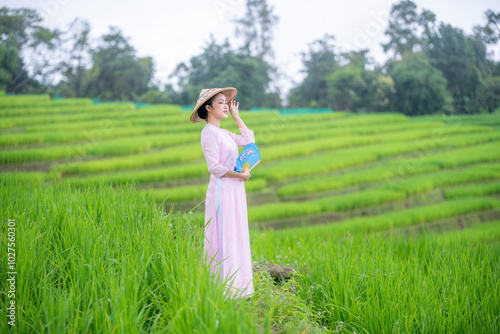 Beautiful women standing in a lush green tea field, likely in a rural area. They are wearing traditional conical hats and light-colored clothing with green tea platation background	 photo