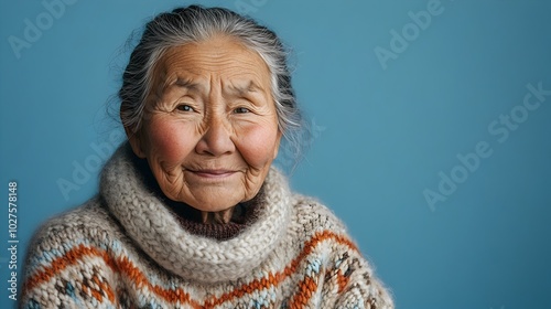 Portrait of a Content and Confident Elderly Inuit Woman Dressed in a Warm Cozy Knitted Sweater Posing Against a Plain Blue Background in a Professional Lighting Studio Setting photo