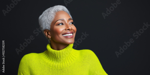 This image showcases a woman with short, gray hair, smiling brightly and wearing a striking, vibrant lime green sweater, against a dark, plain backdrop. photo