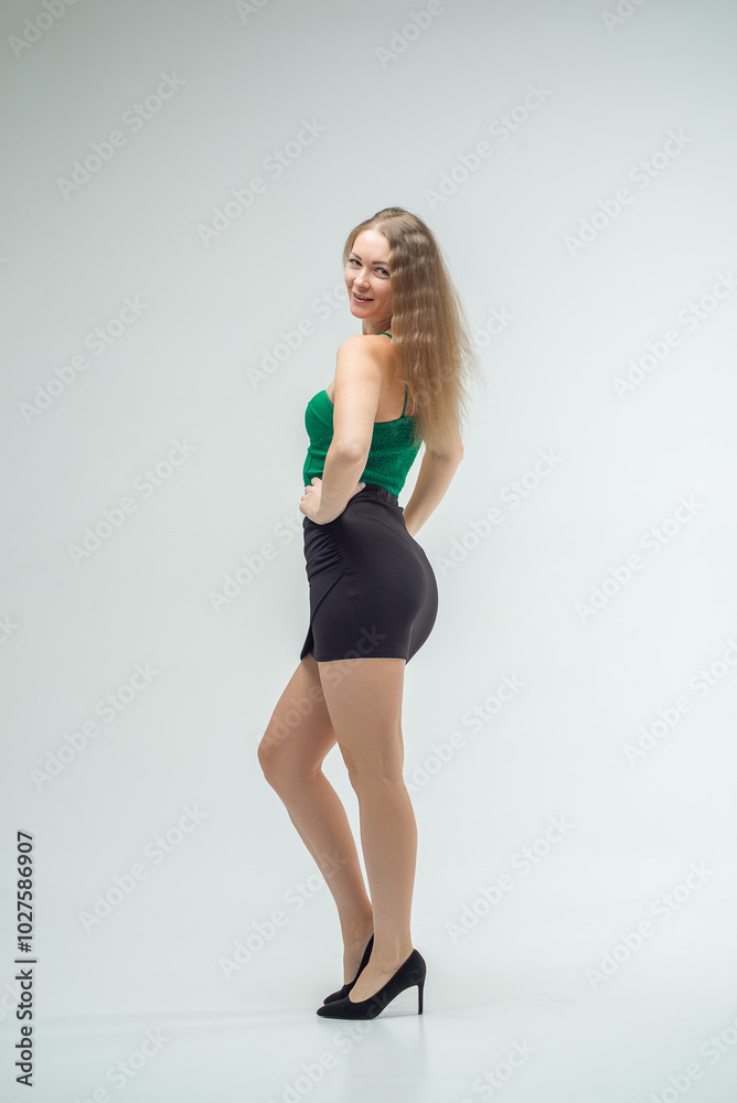 Woman in green top and black skirt posing in front of camera. She has long hair, she is standing on white background. Beautiful sexy body. Fitness and healthy eating concept. Woman in green top and black skirt posing in front of camera. She has long hair, she is standing on white background. Beautiful sexy body. Fitness and healthy eating concept.