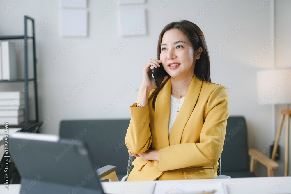 Businesswoman is smiling while talking on her phone and working at her office desk Businesswoman is smiling while talking on her phone and working at her office desk