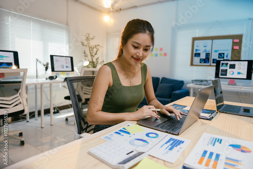 Young professional is analyzing charts and graphs on her computer, developing strategies for success in the modern business world