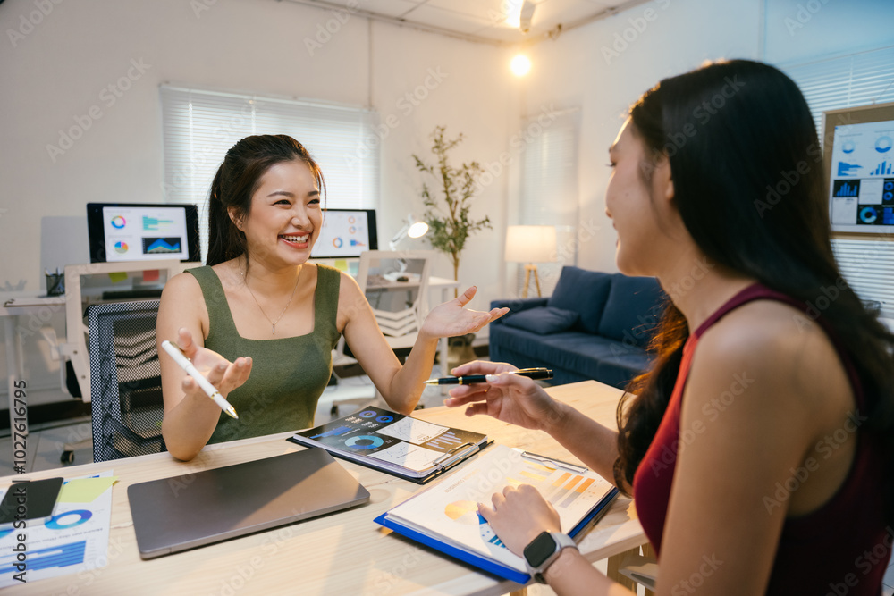 Fototapeta premium Two young businesswomen are discussing about a new project, analyzing statistics on paperwork with charts and graphs while working together at the office