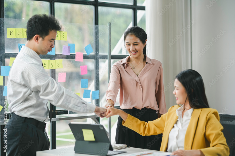 Three asian business people putting their fists together celebrating a business goal achievement in the office Three asian business people putting their fists together celebrating a business goal achievement in the office