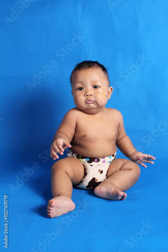 Adorable six month old chubby baby boy learning to sit and play on white background
