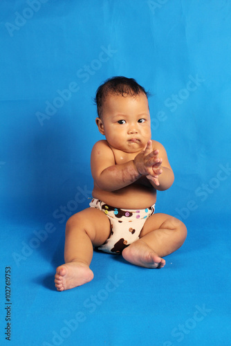 Adorable six month old chubby baby boy learning to sit and play on white background
