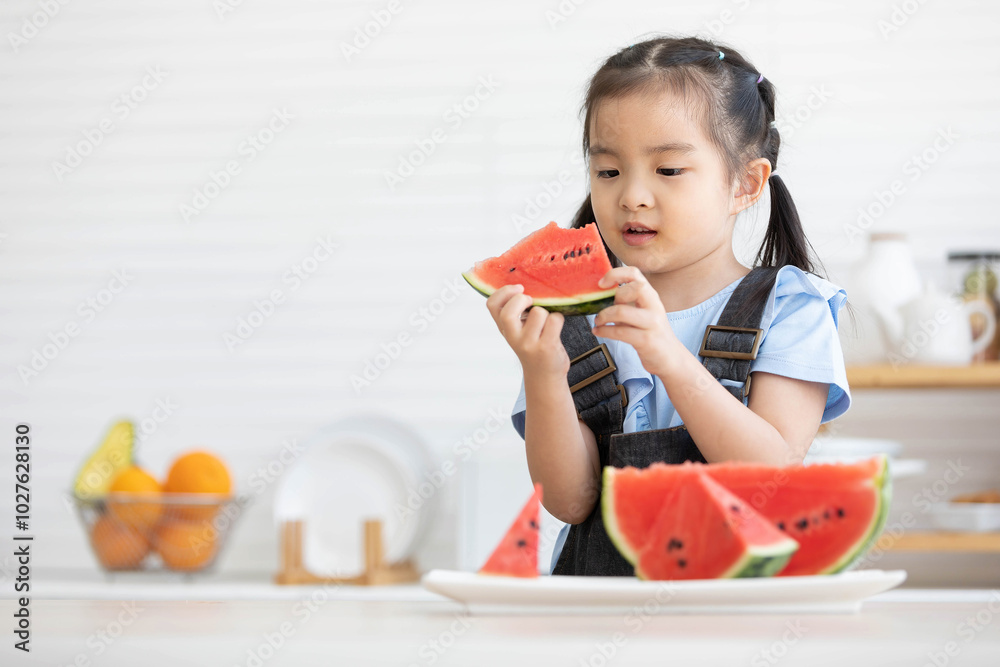 cute asian little child girl eating and looking slice watermelon in the kitchen cute asian little child girl eating and looking slice watermelon in the kitchen