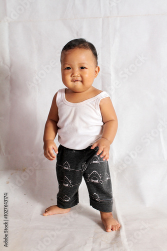 Adorable baby boy practicing standing on white background wearing white bra and shorts for healthy baby advertisement