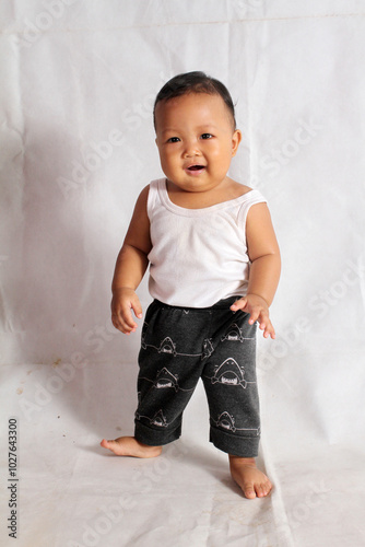 Adorable baby boy practicing standing on white background wearing white bra and shorts for healthy baby advertisement