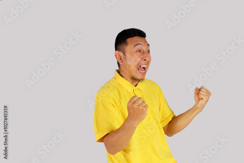 Asian adult man wearing yellow  t-shirt smiling happily after getting a new idea with clenched fist
