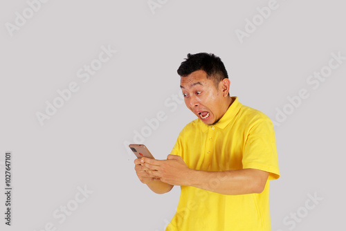 Portrait of an Asian young man looking at his smartphone with an expression of surprise at getting something. Isolated on white background.
 photo