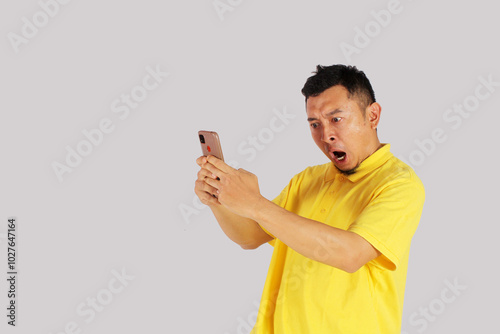 Portrait of an Asian young man looking at his smartphone with an expression of surprise at getting something. Isolated on white background.
