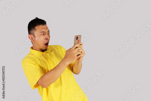 Portrait of an Asian young man looking at his smartphone with an expression of surprise at getting something. Isolated on white background.
