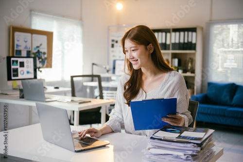 Smiling asian businesswoman works on her laptop in the office, analyzing marketing data and handling paperwork with a focus on corporate success Free Download Smiling asian businesswoman works on her laptop in the office, analyzing marketing data and handling paperwork with a focus on corporate success - GFXLoad
