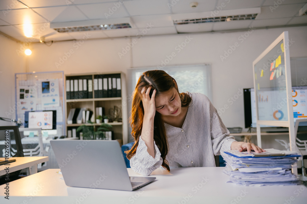 Businesswoman having headache, touching her head, feeling tired and stressed from overload work with many documents and laptop on table Businesswoman having headache, touching her head, feeling tired and stressed from overload work with many documents and laptop on table