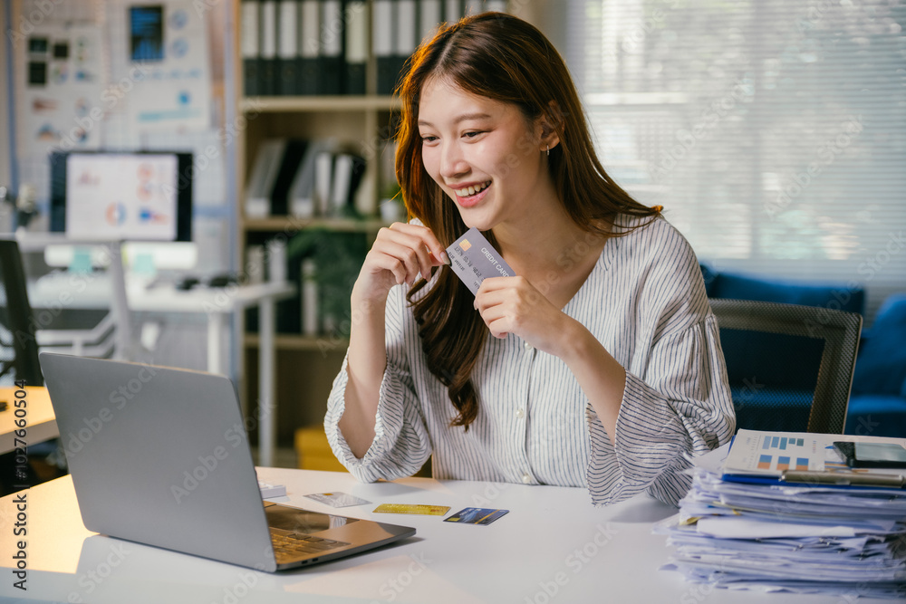 Smiling entrepreneur makes an online purchase with a credit card on her laptop at the office, showcasing modern e-commerce Smiling entrepreneur makes an online purchase with a credit card on her laptop at the office, showcasing modern e-commerce