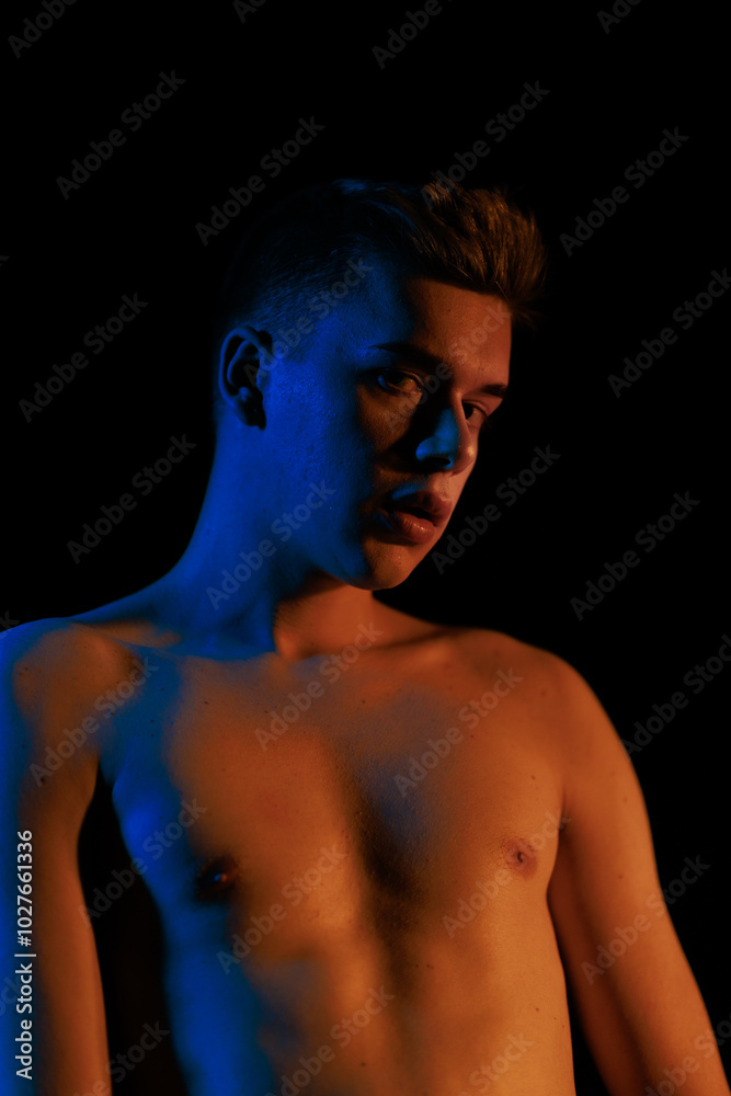 Young man posing in the dark with red and blue light in the studio Young man posing in the dark with red and blue light in the studio