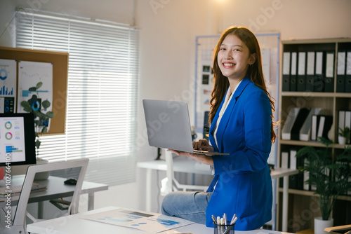 Young manager exudes confidence and joy while working on her laptop in a modern office setting, embodying success and professionalism