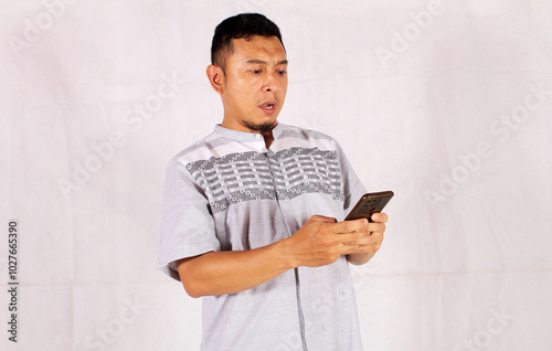 Adult Asian man showing sad and thinking feelings while looking at his cell phone