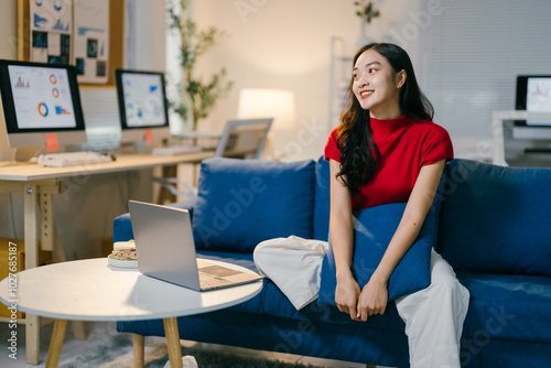 Young asian female freelancer is enjoying a relaxing break on a comfortable blue sofa in her home office, taking a moment for herself amidst a productive workday