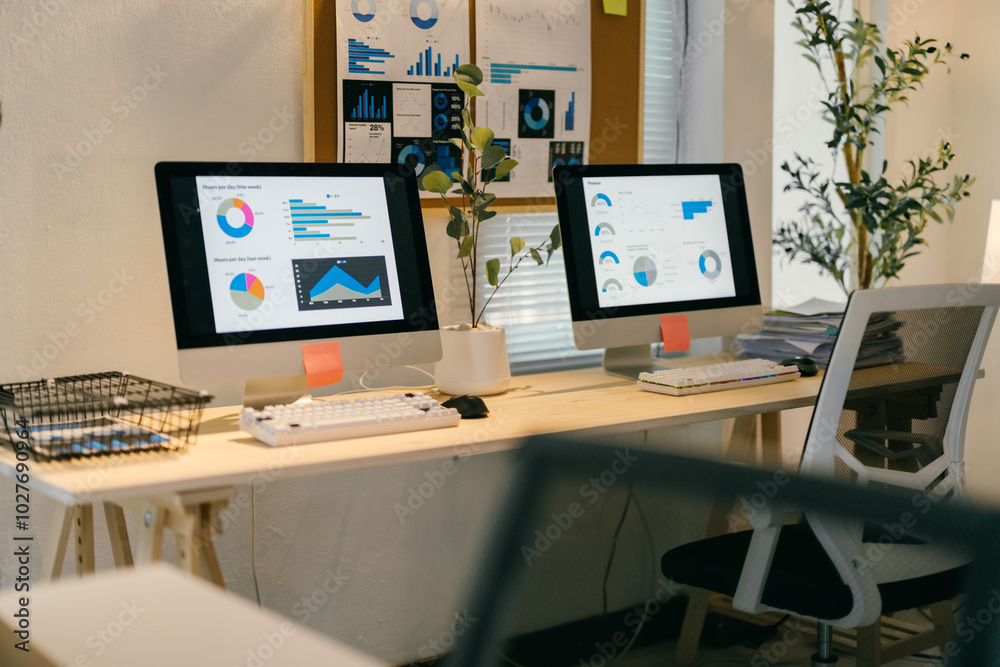 Two desktop computers are displaying financial data and charts on a desk in a modern office, suggesting a focus on data analysis and financial performance Two desktop computers are displaying financial data and charts on a desk in a modern office, suggesting a focus on data analysis and financial performance