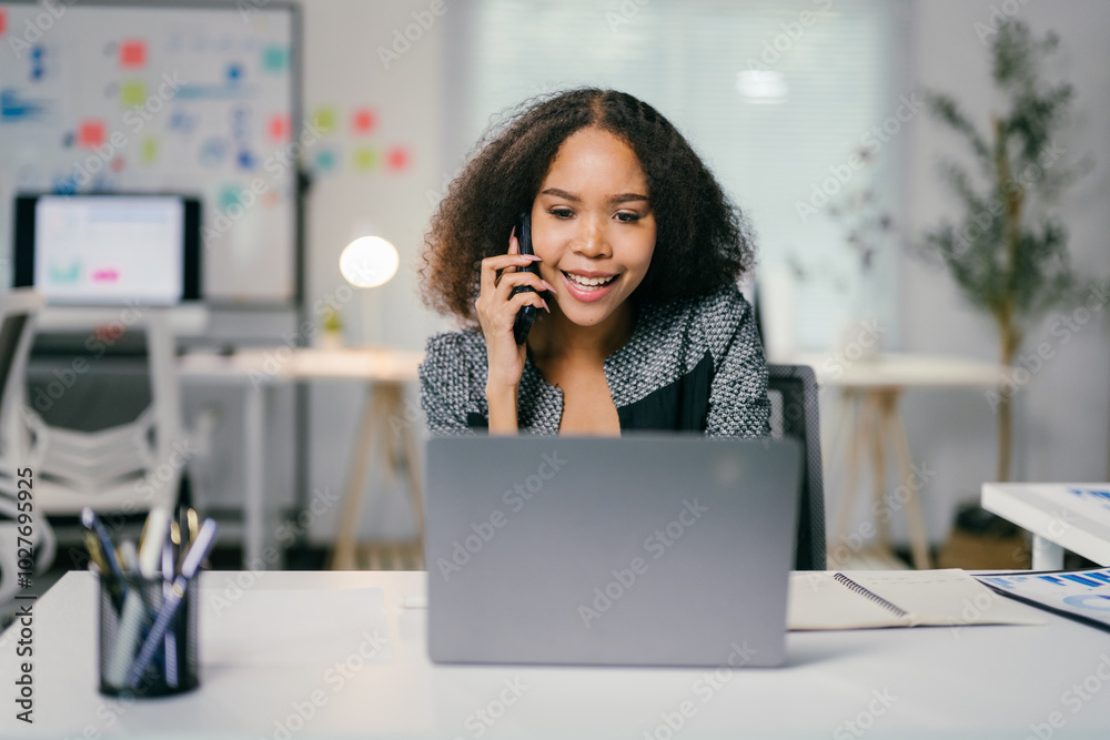Smiling businesswoman multitasks on her laptop and phone in a bright office, showcasing diversity and ambition Smiling businesswoman multitasks on her laptop and phone in a bright office, showcasing diversity and ambition