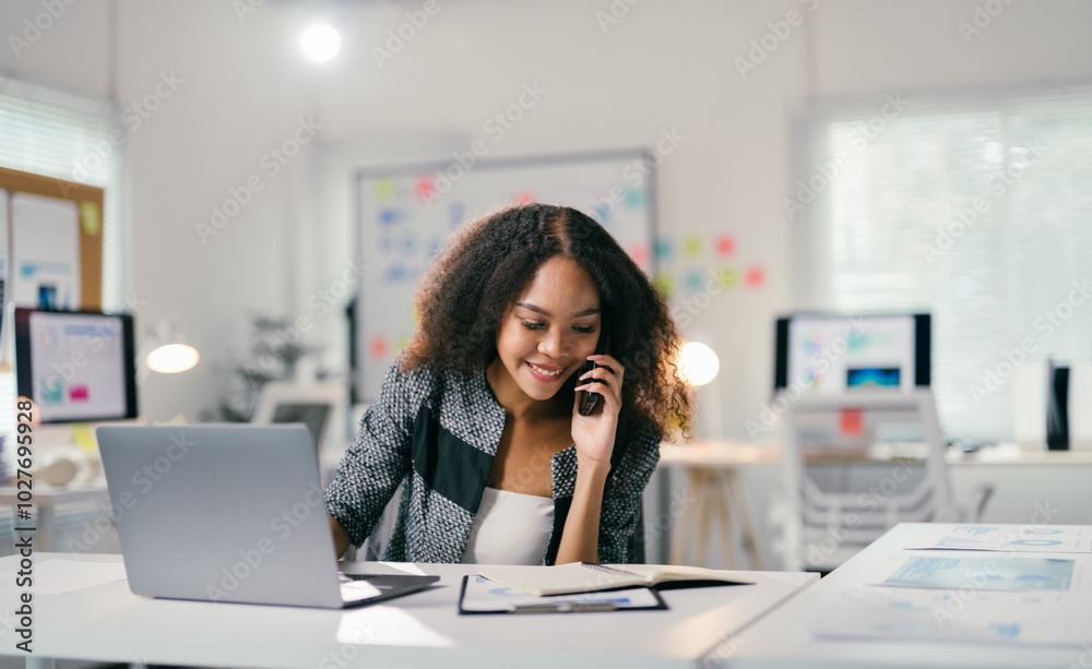 Young manager is working in a luminous open space and handling business on the phone, she is smiling and seems focused Young manager is working in a luminous open space and handling business on the phone, she is smiling and seems focused