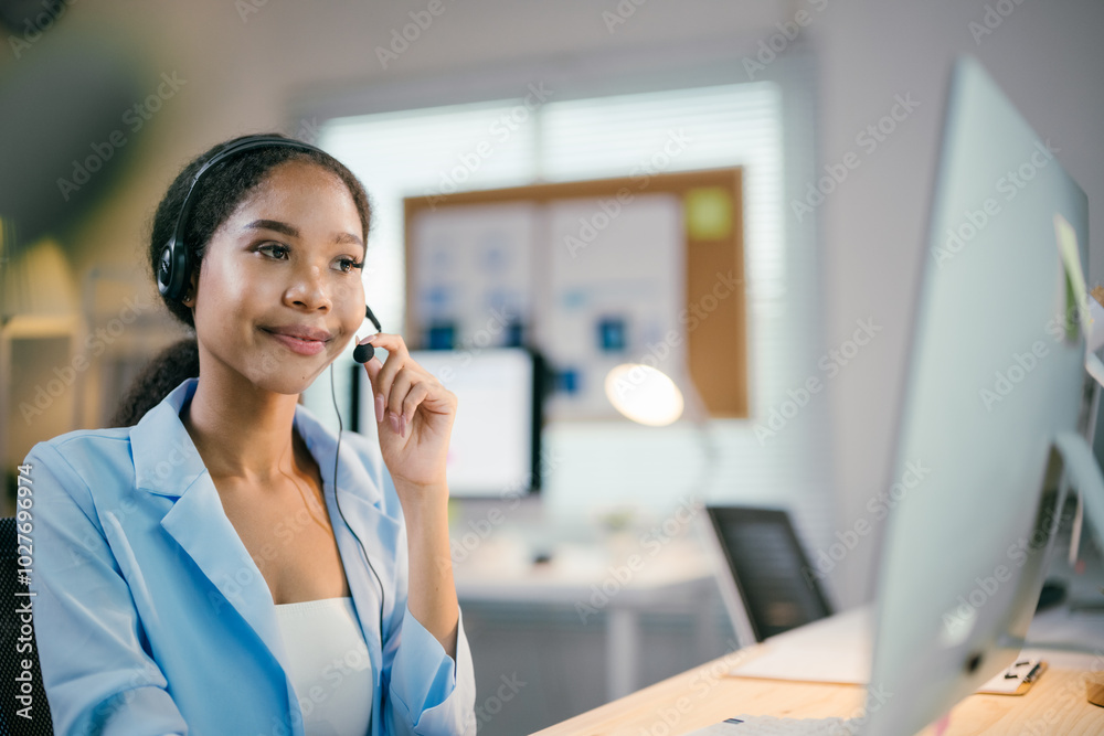 African american businesswoman is working in her office, wearing a headset and smiling while looking at her computer screen African american businesswoman is working in her office, wearing a headset and smiling while looking at her computer screen